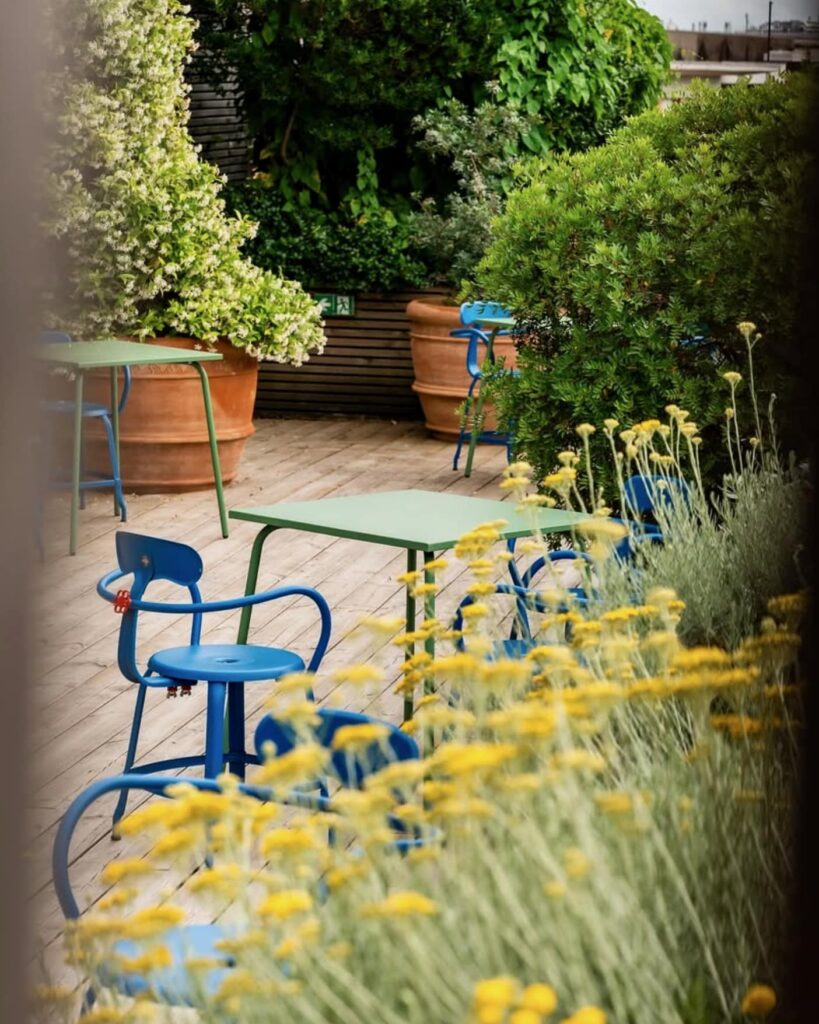 Terrasse verdoyante avec Fauteuil outdoor by Paola Navone et tables colorées