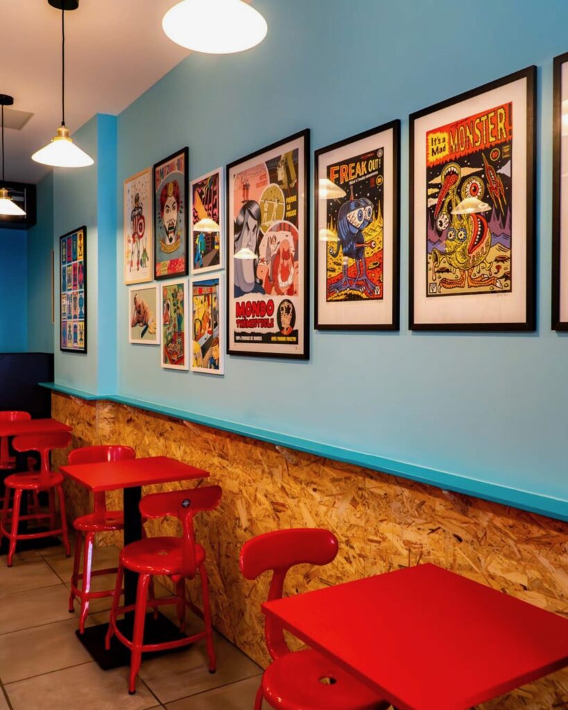 Restaurant italien coloré avec chaises Nicolle rouge et affiches artistiques.